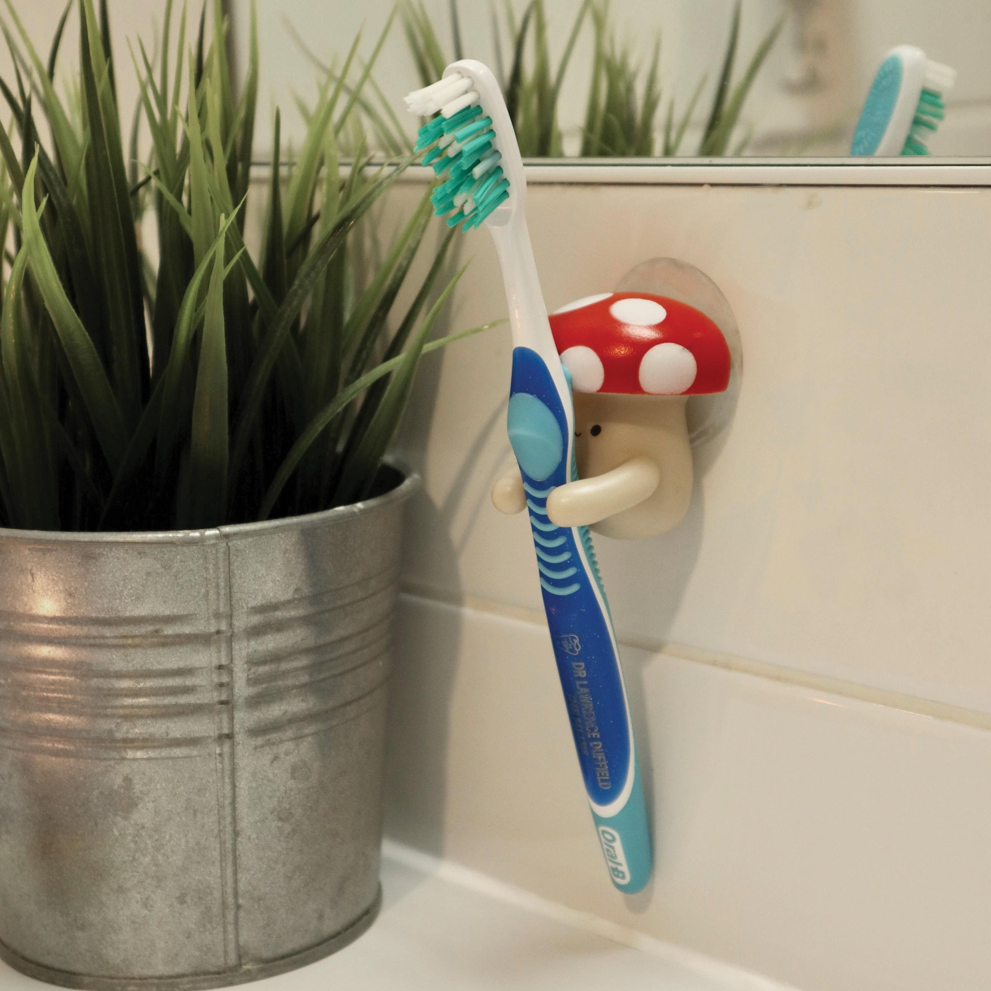 Mushroom  shaped toothbrush holder holding a blue tooth brush on a tiled background