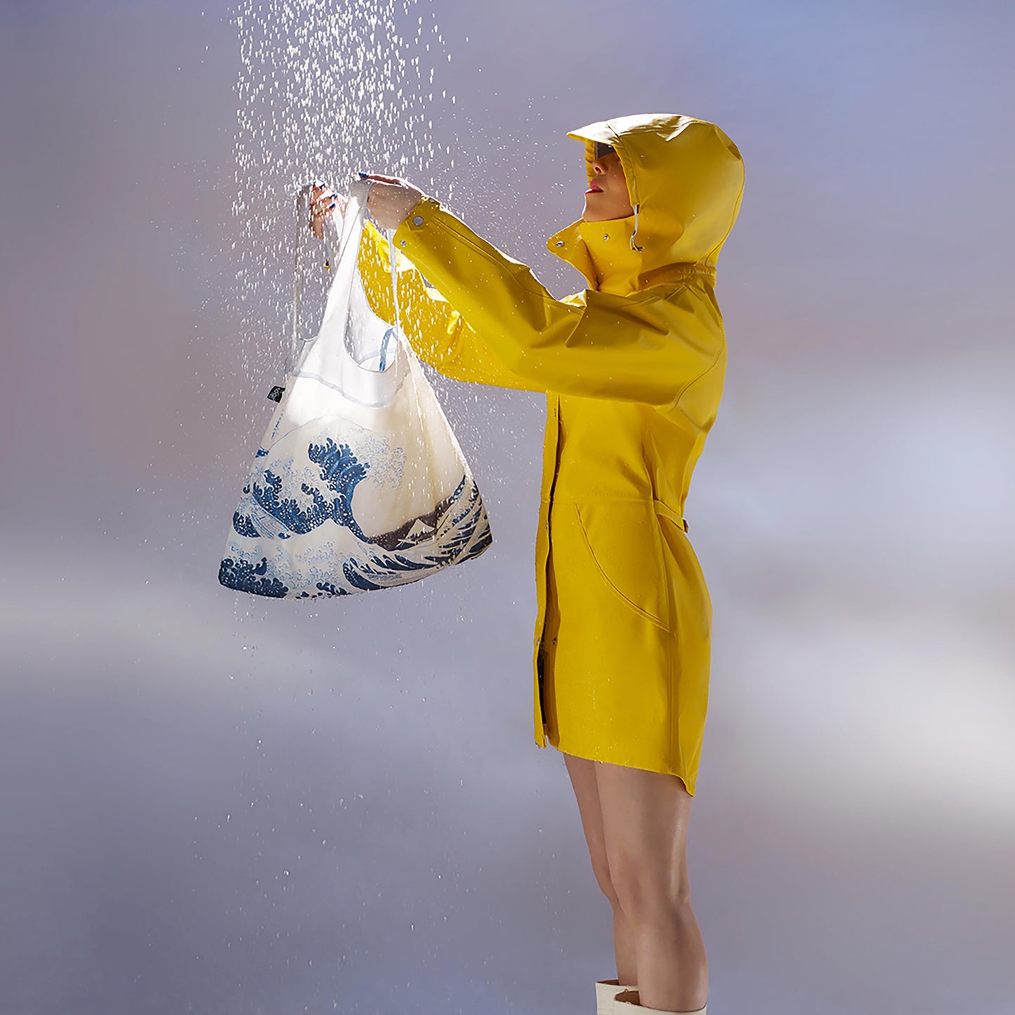 A person in a yellow raincoat catching rainfall in the shopping bag. The background is grey.