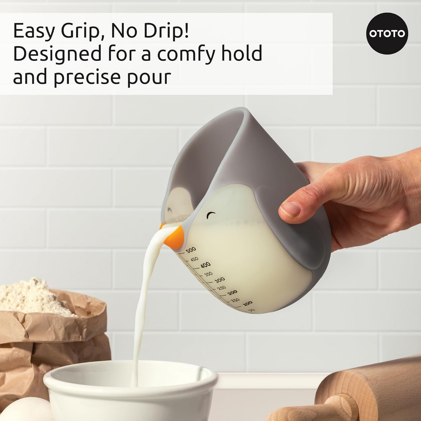 A hand pouring milk from the penguin shaped measuring cup into a bowl.