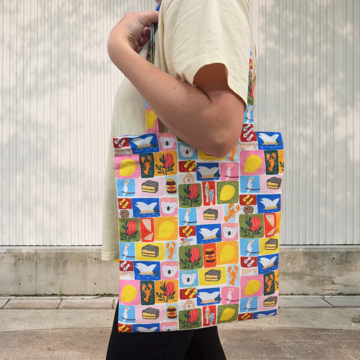 Person holding a Suki Mcmaster Aussie Icons tote bag with various patterns against a neutral background