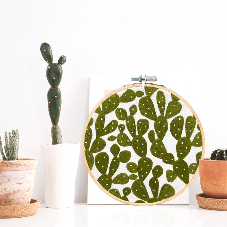 Lifestyle picture.Completed embroidery needlecraft of: Prickly pears placed amongst cactii planters.