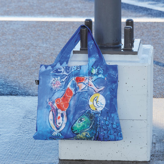 Colorful tote bag with artistic design leaning against a pole on a street.