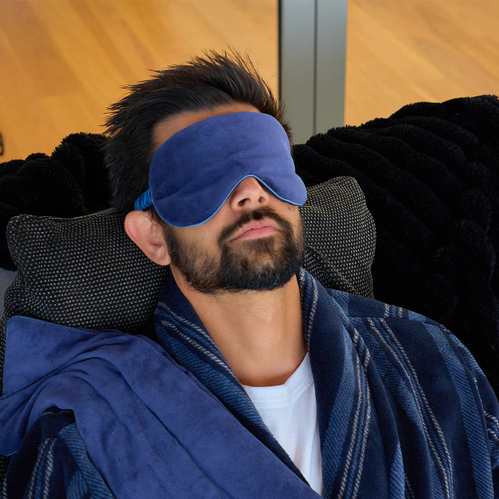 Man wearing a blue sleep mask and robe, sitting on a black couch.