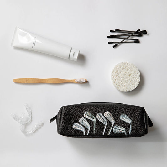 Black toiletry bag with white designs surrounded by a toothbrush, tube of toothpaste, cotton swabs, and sponge on a light gray background.