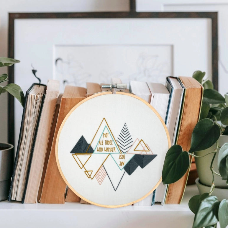 An Embroidery hoop leaning amongst a stack of books and green foliage.