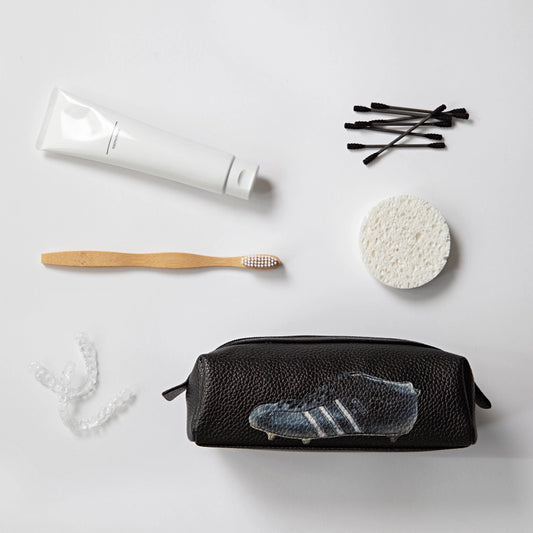 Black toiletry bag with Adidas logo, toothbrush, toothpaste, and other travel items on a light gray background