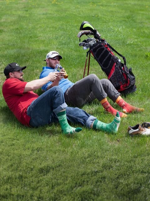 Two golfers laying down on the grass and toasting their beers as they wear BLUEQ men’s crew socks -Gizmo Gifts