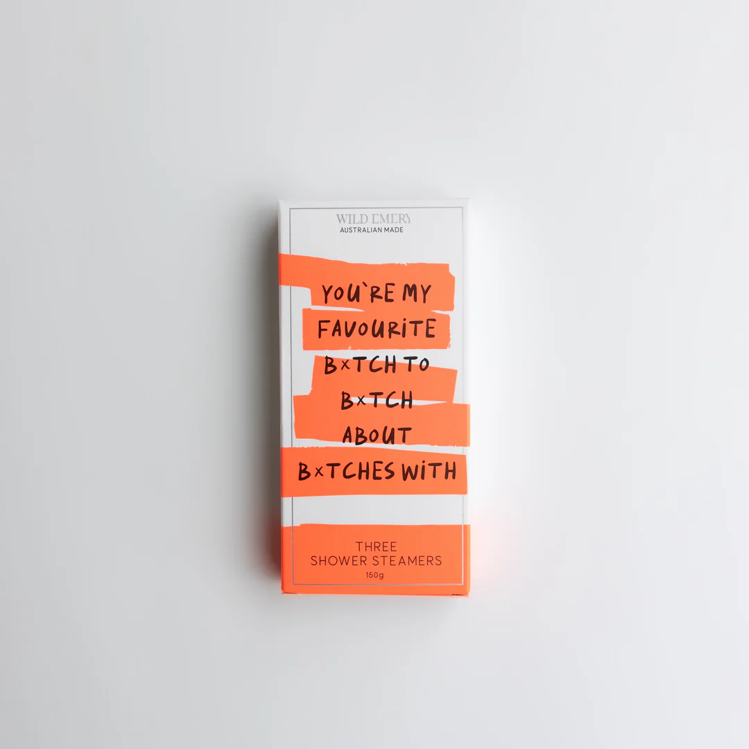 An orange package containing a trio of Wild Emery scented shower steamers. Slogan reads: You're my favourite b*tch to B*tch about b*tches with. Background is white.