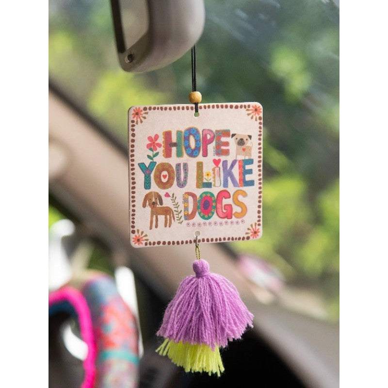 Decorative car hanging with 'Hope you like dogs' text and tassels, hanging from a car's rearview mirror.