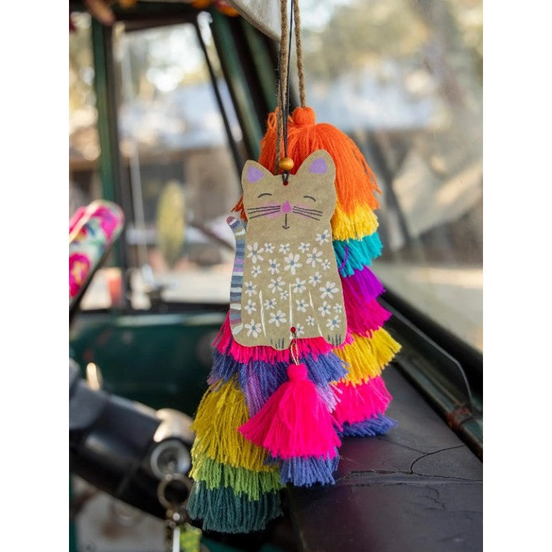 A colorful cat-shaped car hanging air freshenerwith a beige patterned body, orange tassel hair, and layered rainbow tassels, hanging in a vehicle interior.