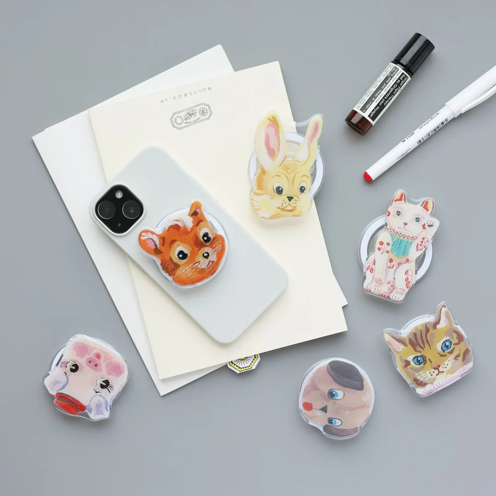 Set of animal-themed phone grips and  gray surface with stationery items.