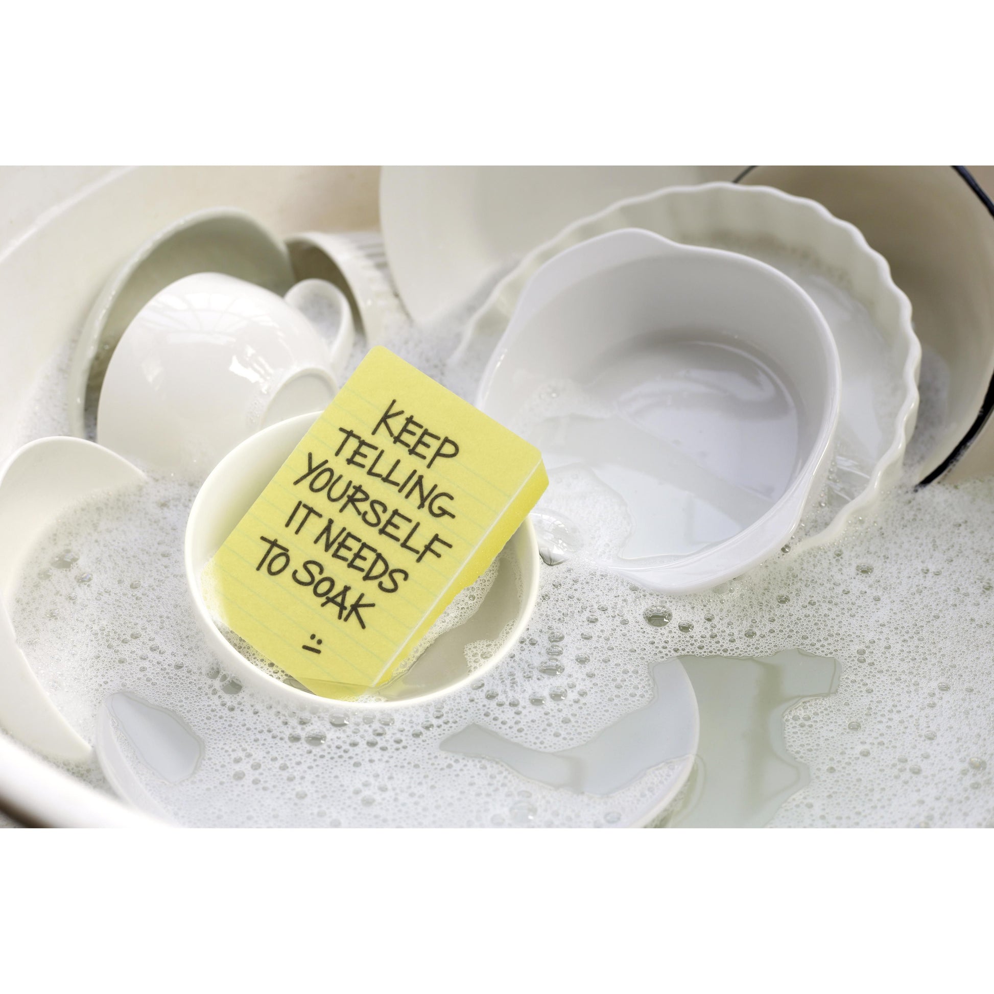 a yellow sponge with text in a soapy kitchen sink with dishes