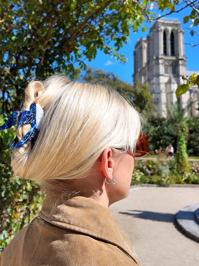 Person with blonde hair and a blue Swallow  hair accessory, looking towards a cathedral.