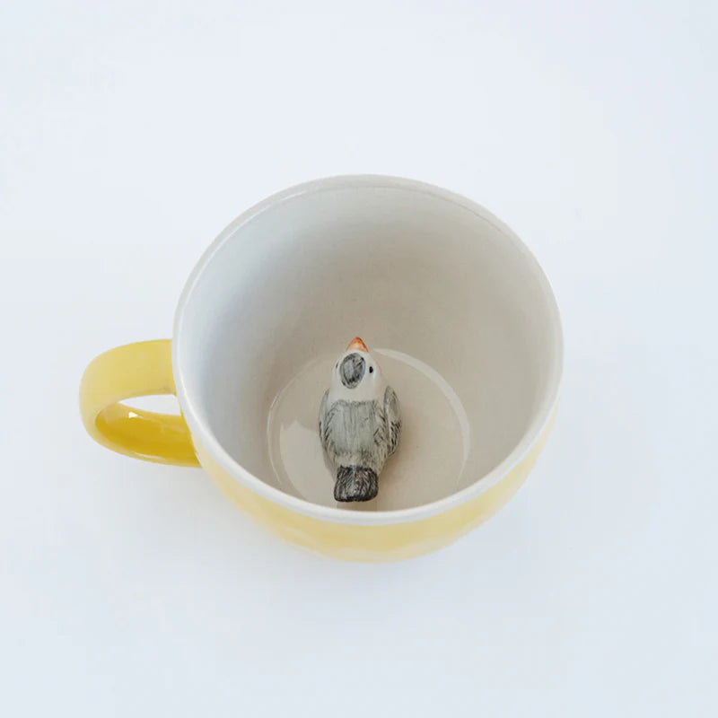 Small  bird figurine inside a yellow mug on a white background