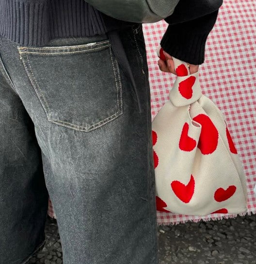 Person holding a white bag with red hearts against a red and white checkered background