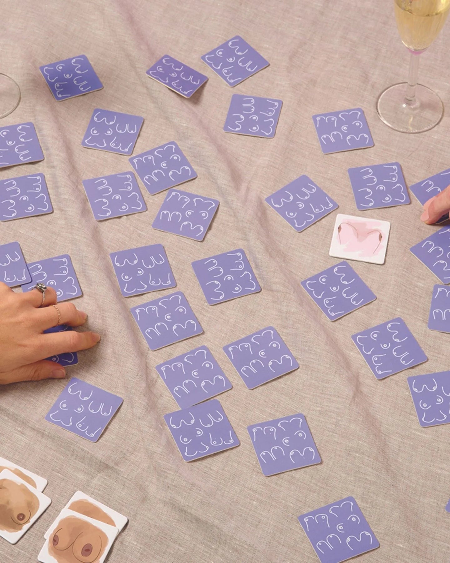 Purple cards with breast illustrations on a beige surface, with hands interacting with the cards.