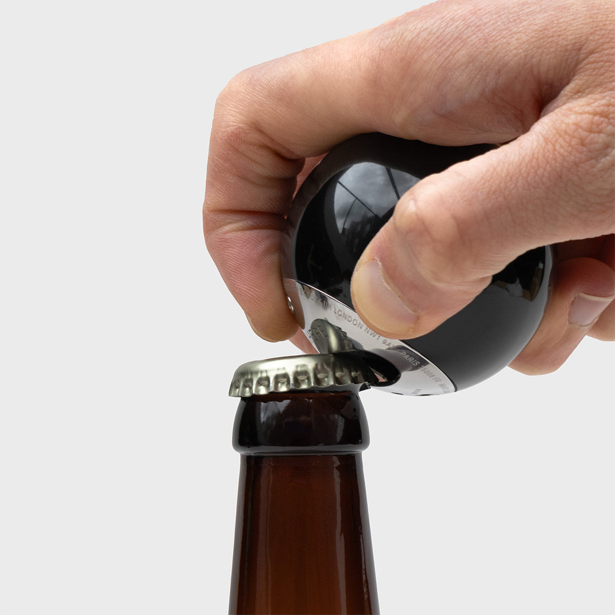 A hand using the 8 ball bottle opener to open a beer cap of a bottle.