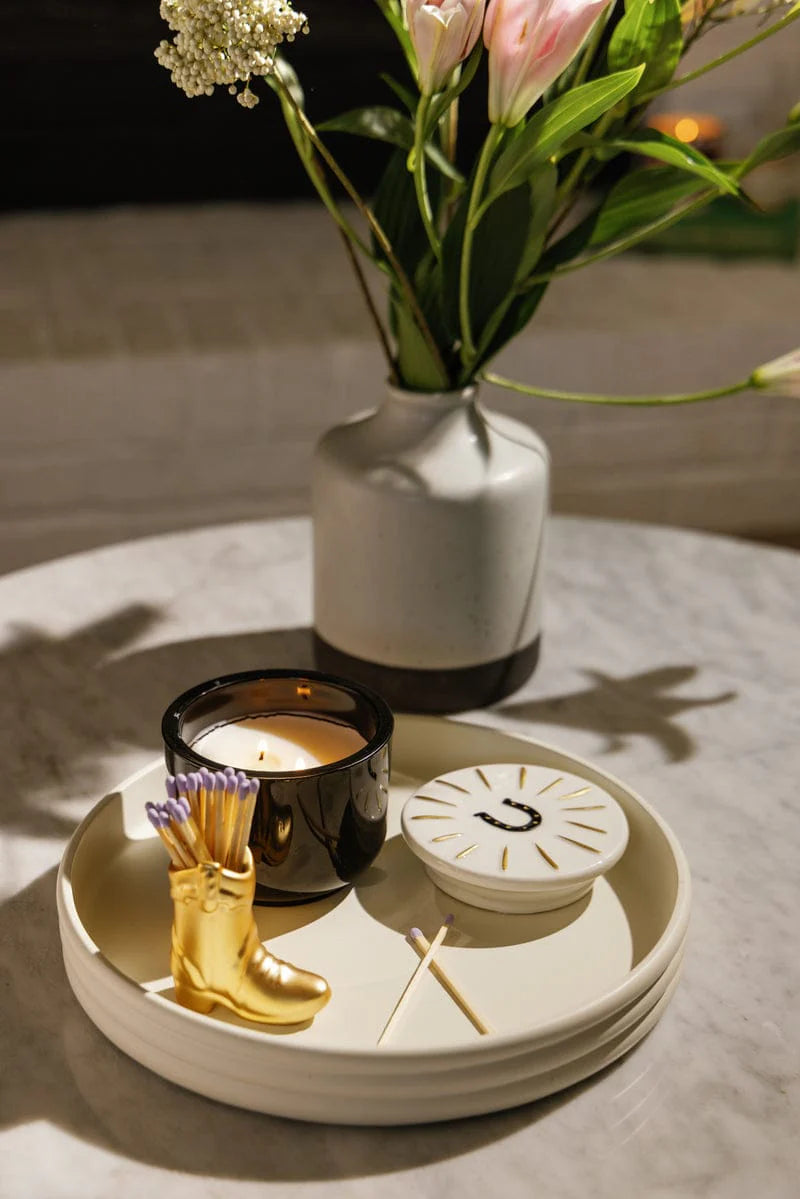 Decorative items including a candle, gold boot, and white vase with flowers on a table.