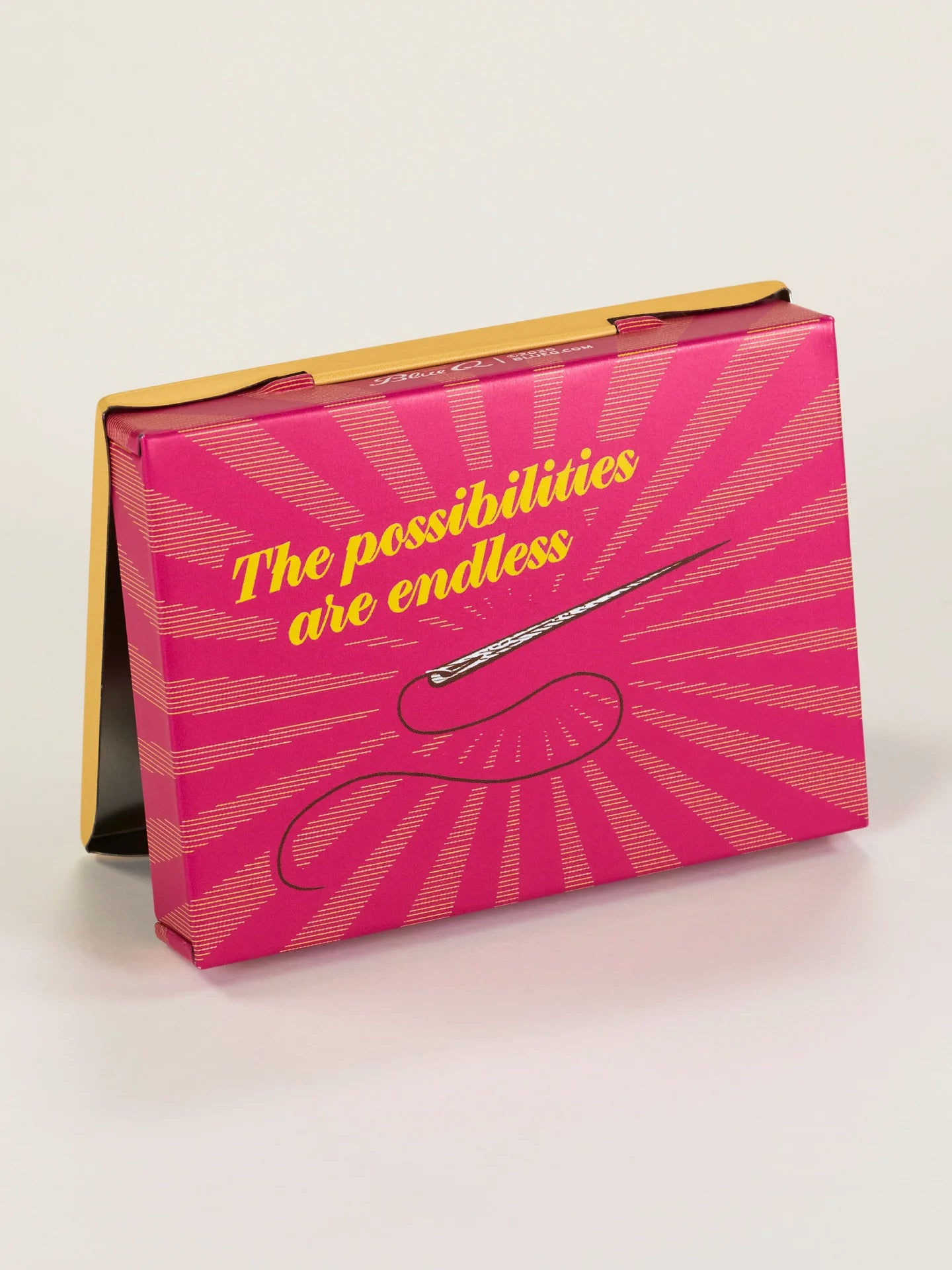 Back view of a pocket size Pins and Needles tin box. It features a bright pink  background with a picture of a needle and a yellow font that reads: The possibilities are endless.