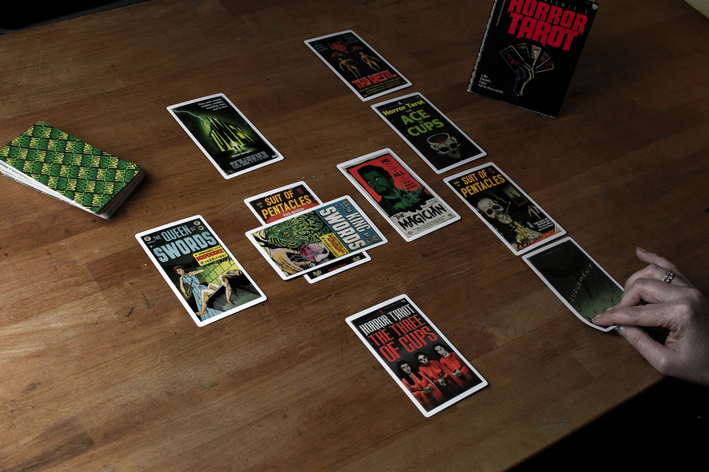 Horror-themed tarot cards on a wooden table with a hand reaching for a card.