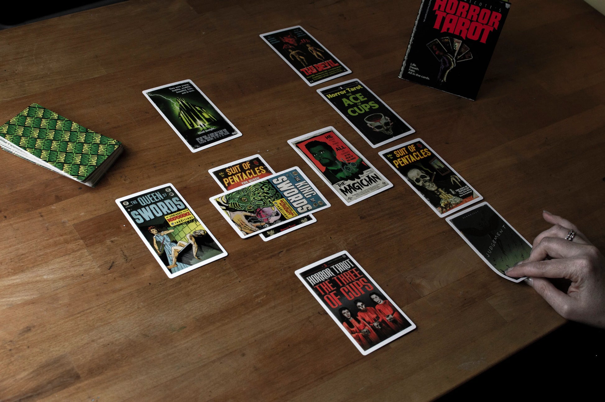 Horror-themed tarot cards on a wooden table with a hand reaching for a card.