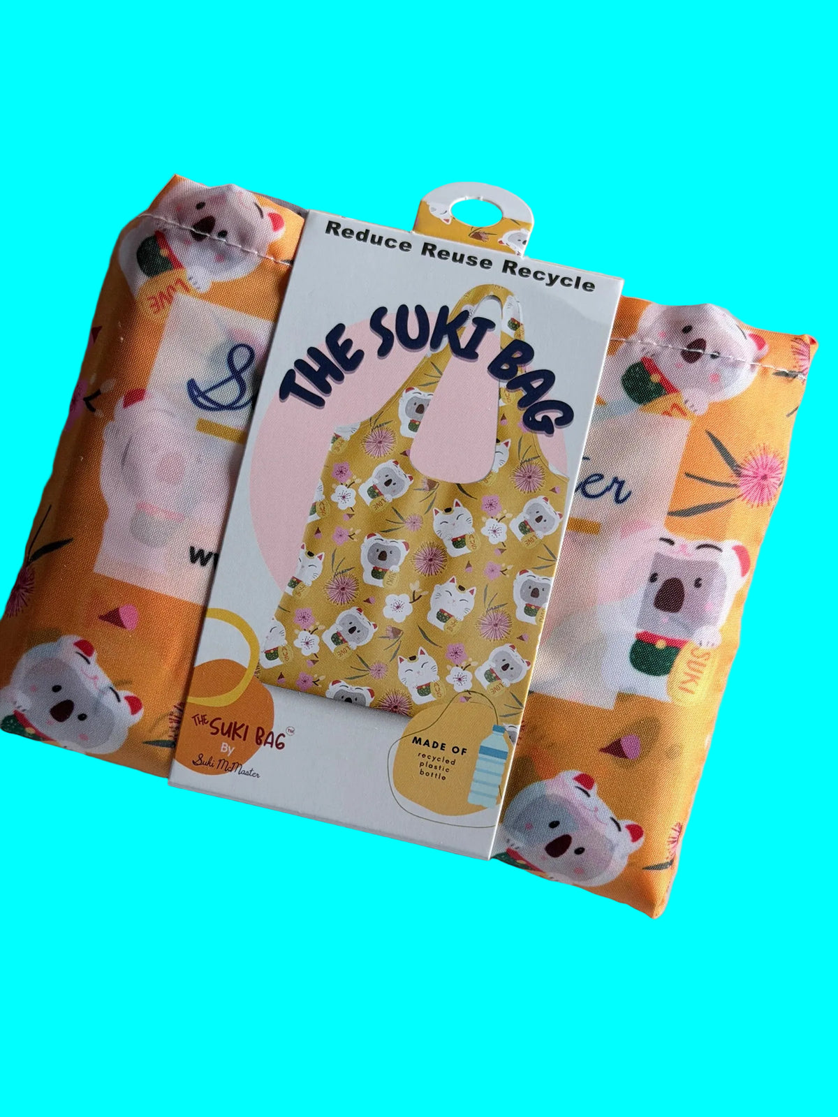 A yellow folded shopping bag with a paper band and text that reads: The Suki Bag. The background is aqua blue.