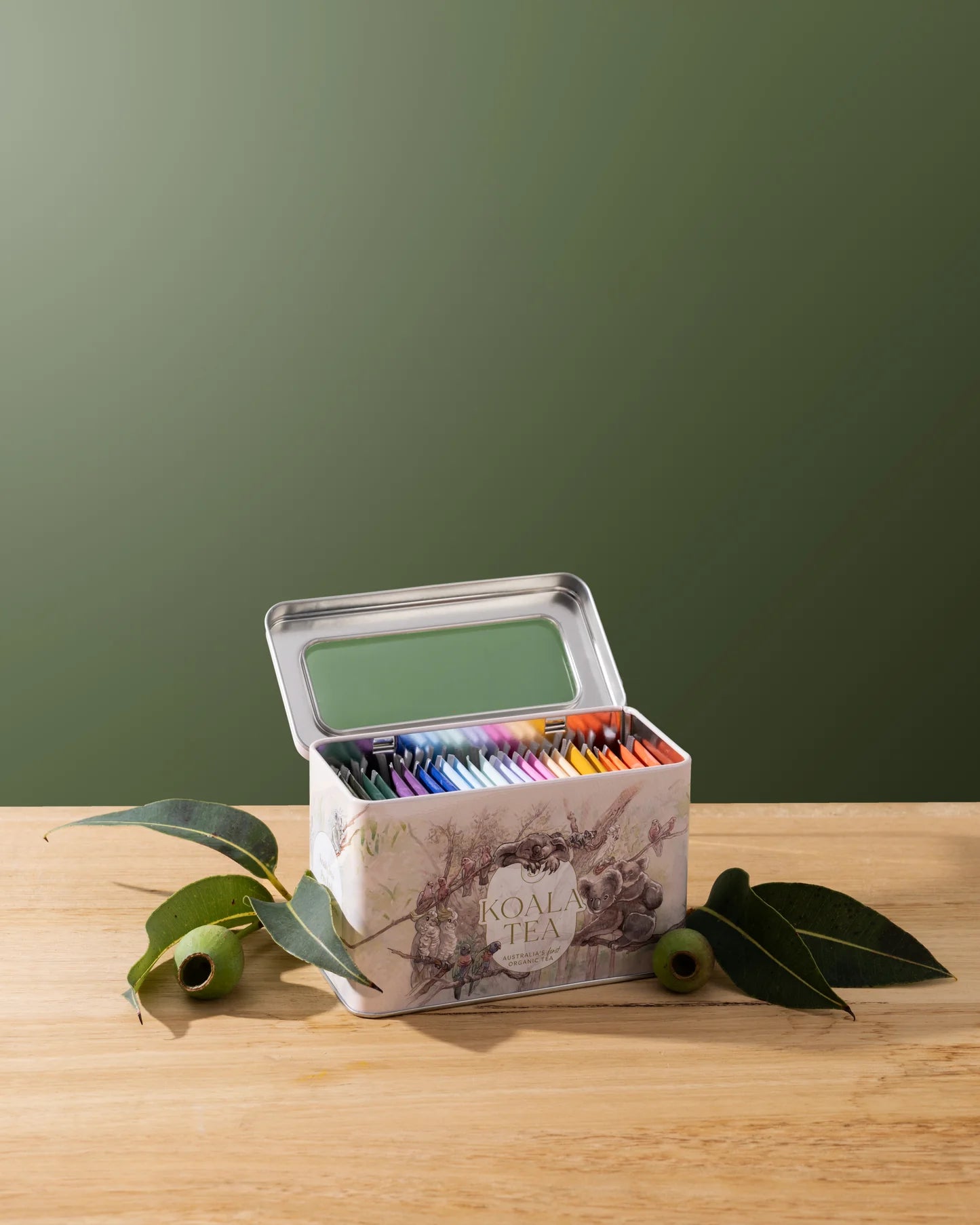 Set of colored pencils in a tin box on a wooden surface with a green background
