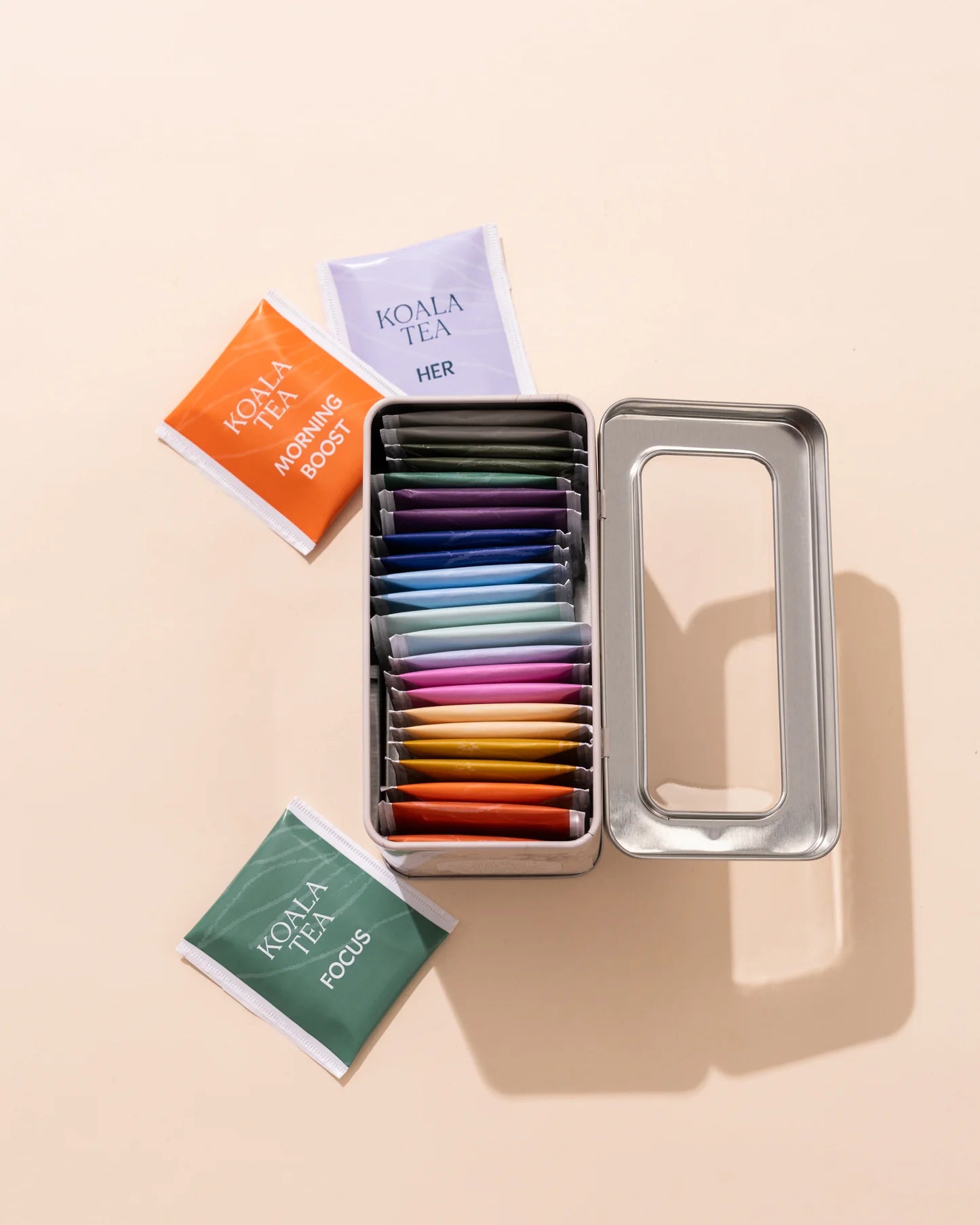 Assorted Koala Tea packages in a metal tin on a beige background
