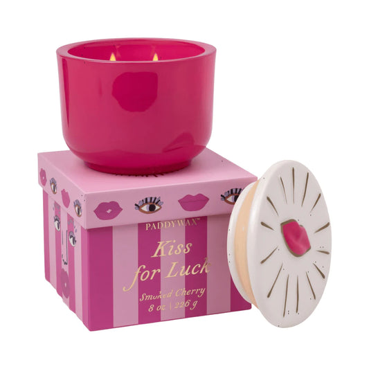 Pink candle in a striped box with 'Kiss for Luck' text, surrounded by decorative elements.