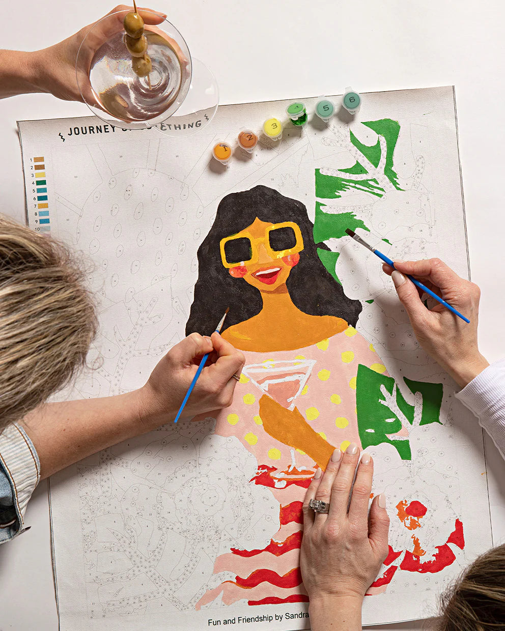 Two people painting a colorful illustration of a woman on a white surface.