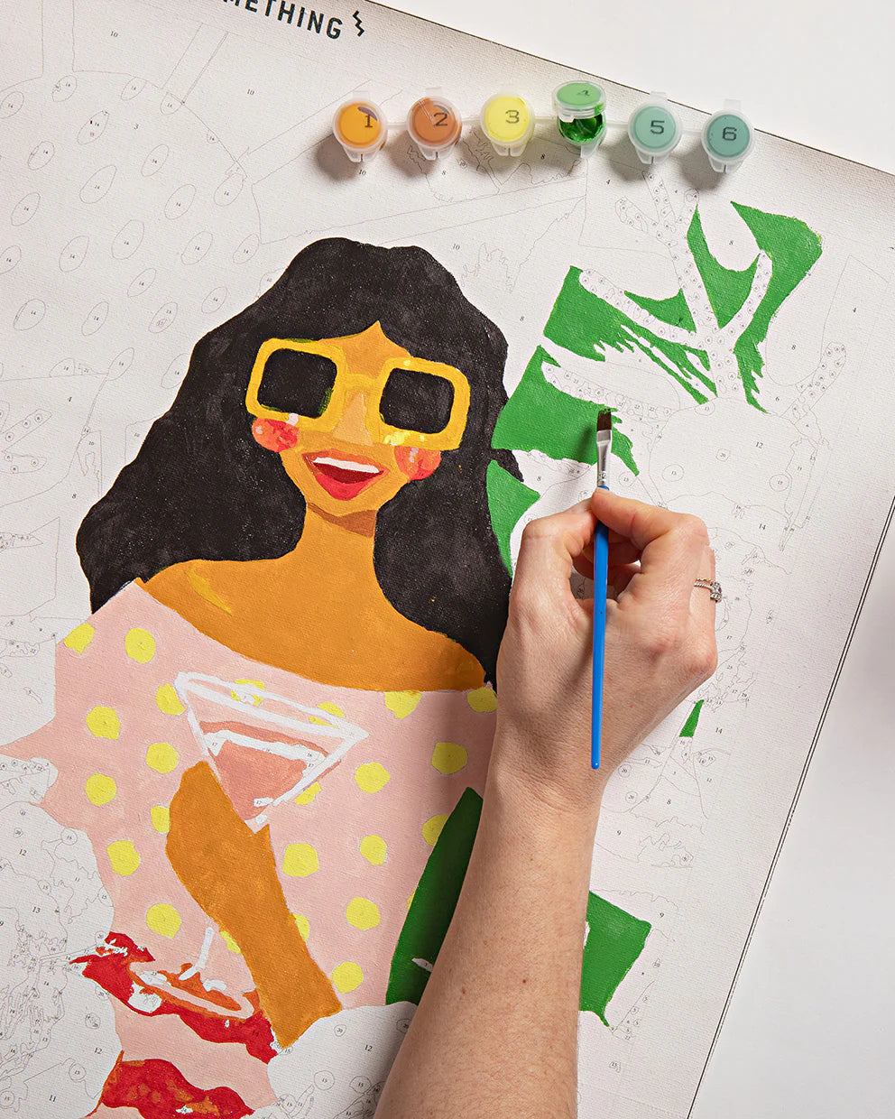 Person painting a colorful illustration of a woman with sunglasses on a white board.