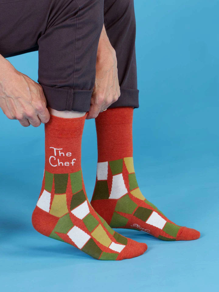 A person pulling up a pair of "The Chef" crew socks on a bue background.
