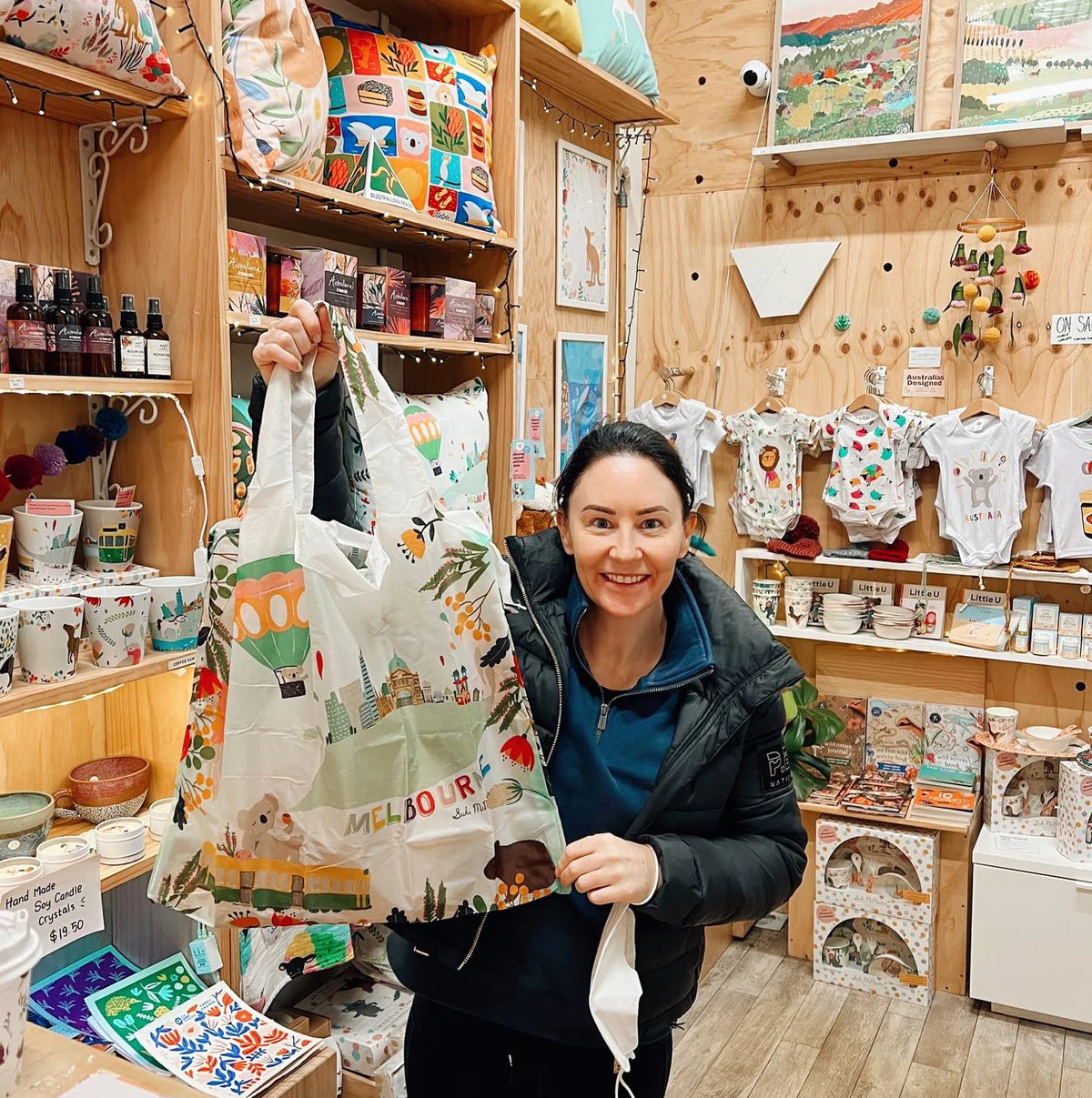A woman in a gift shop holding up a shopping bag that is printed with Melbourne icons.