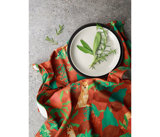 Red and green patterned cloth featuring an Australian Dingo dog with a white plate holding green leaves on a gray surface.