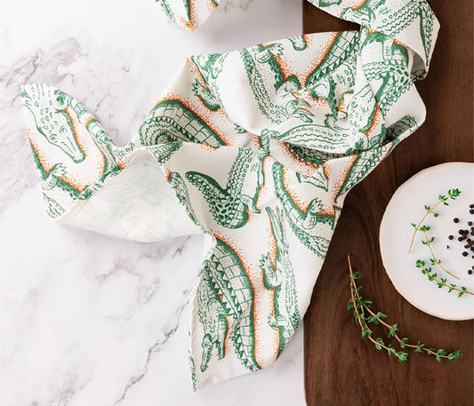 a scattered crocodile print tea towel on a marble table , a wooden side table featuring a plate and lemon myrtle twigs