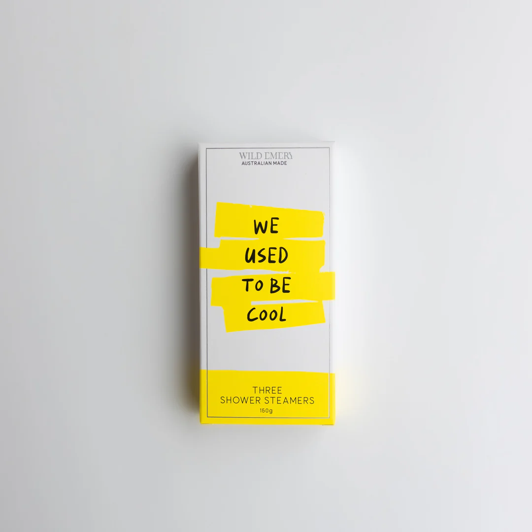 A yellow box  containing a trio of Wild Emery shower steamers. Slogan reads: We used to be cool. Background is white.