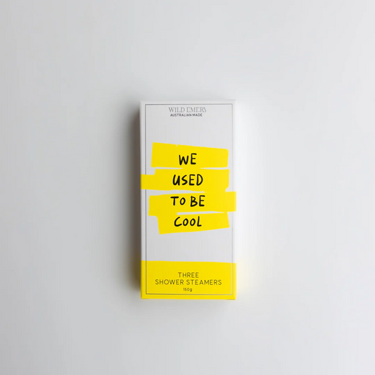 A yellow box  containing a trio of Wild Emery shower steamers. Slogan reads: We used to be cool. Background is white.