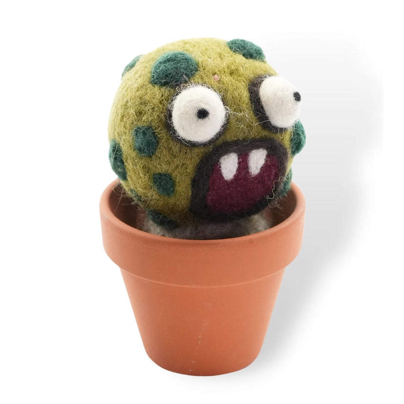 A round wool felt barrel cactus with googly eyes and an opened mouth with two fangs. The decoration sits in a terracotta pot and, the background is white.