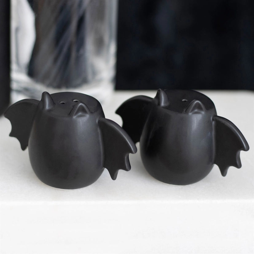 A set of two black bat winged salt and pepper shakers on a photographic background.
