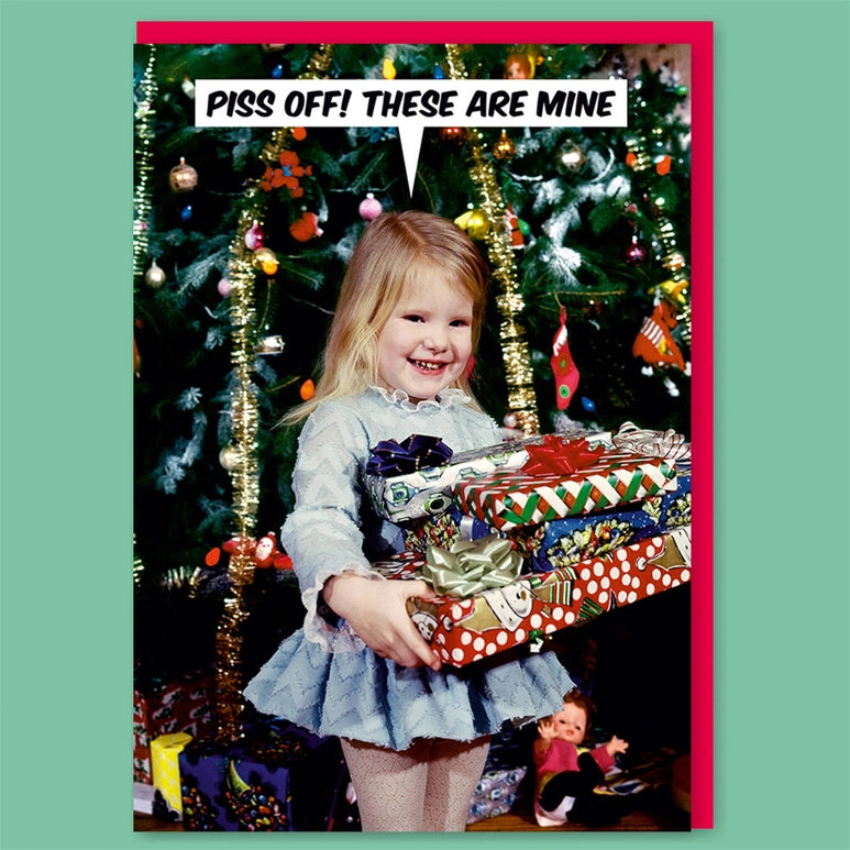 Child holding Christmas presents with a humorous text bubble in front of a decorated tree.