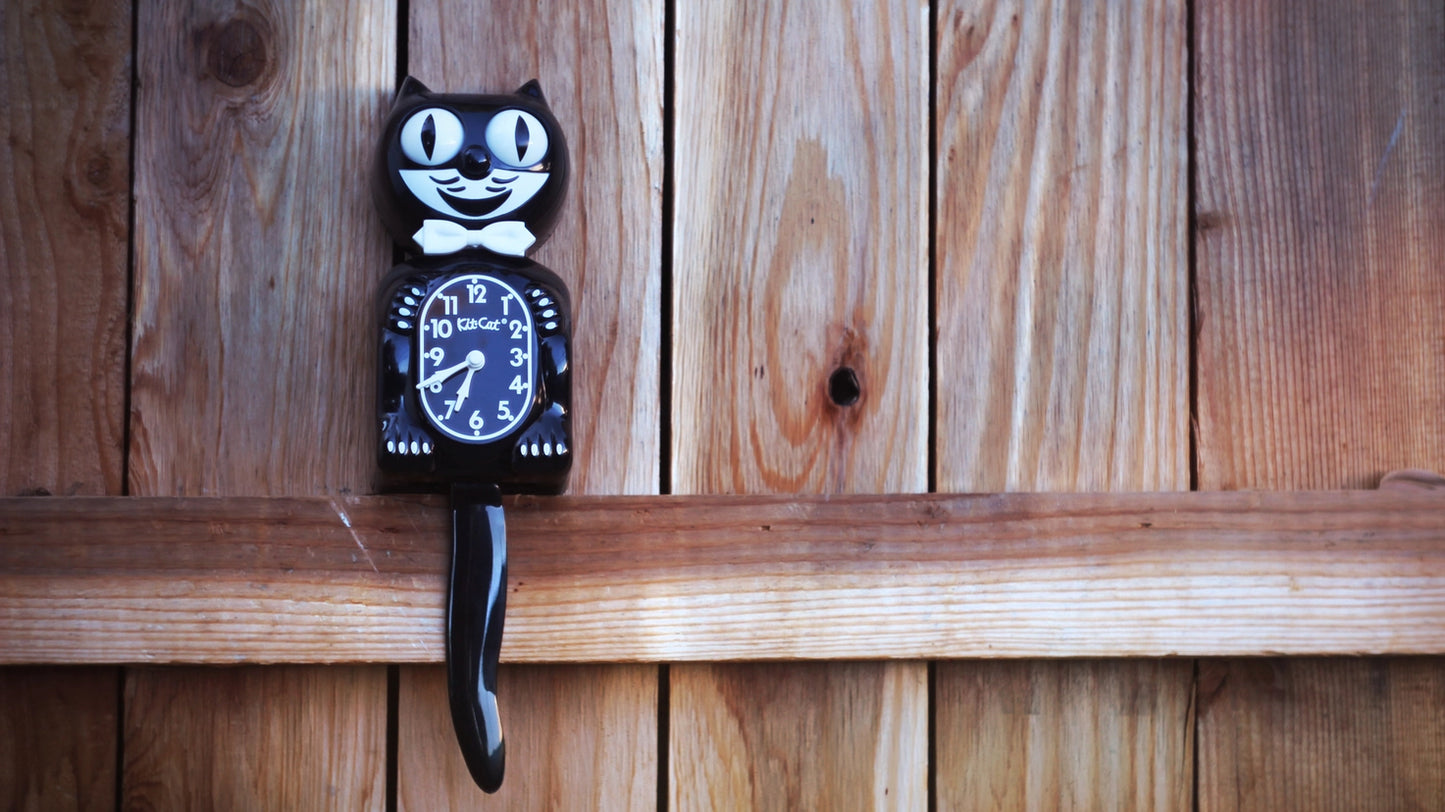 Black cat-shaped clock with a white face on a wooden surface