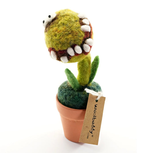 A green felt decoration in the shape of a potted cactus. It has yes an a creepy toothy grin. A label at the bottom of the brand reads: Woolbuddy. The background is white.