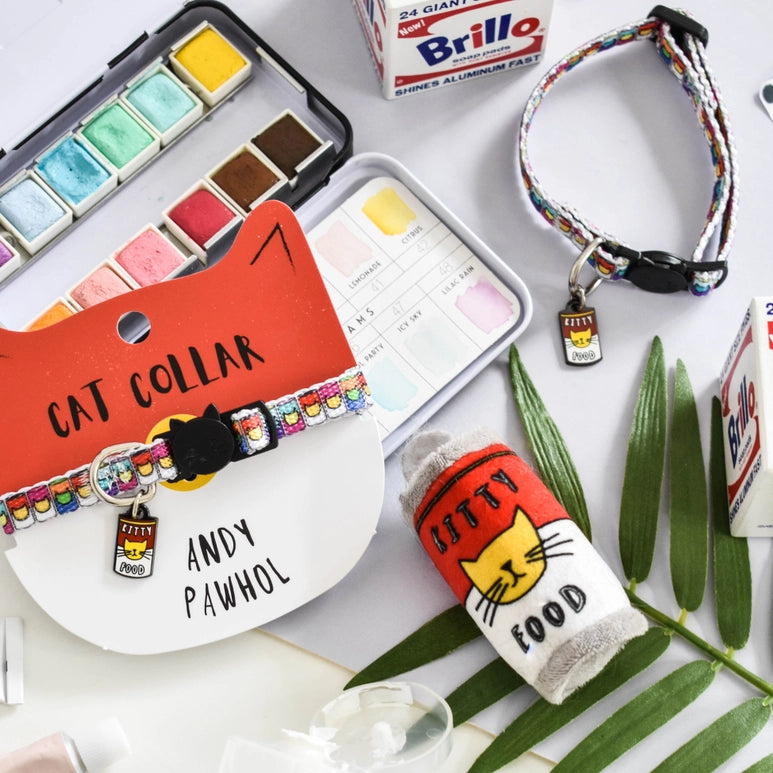 Cat collar, 'Kitty Food' pouch, and watercolor set on a white surface with leaves.