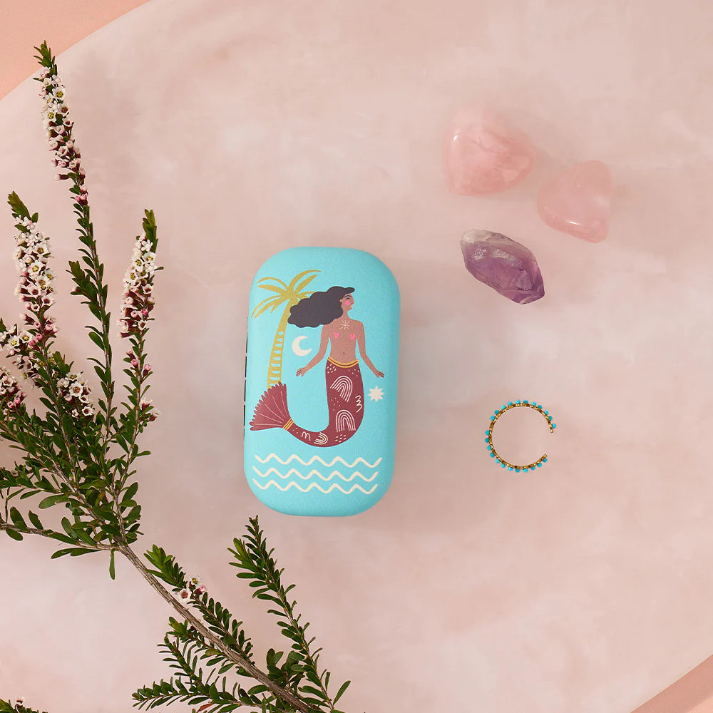 Blue case with mermaid illustration on a pink surface with flowers and crystals