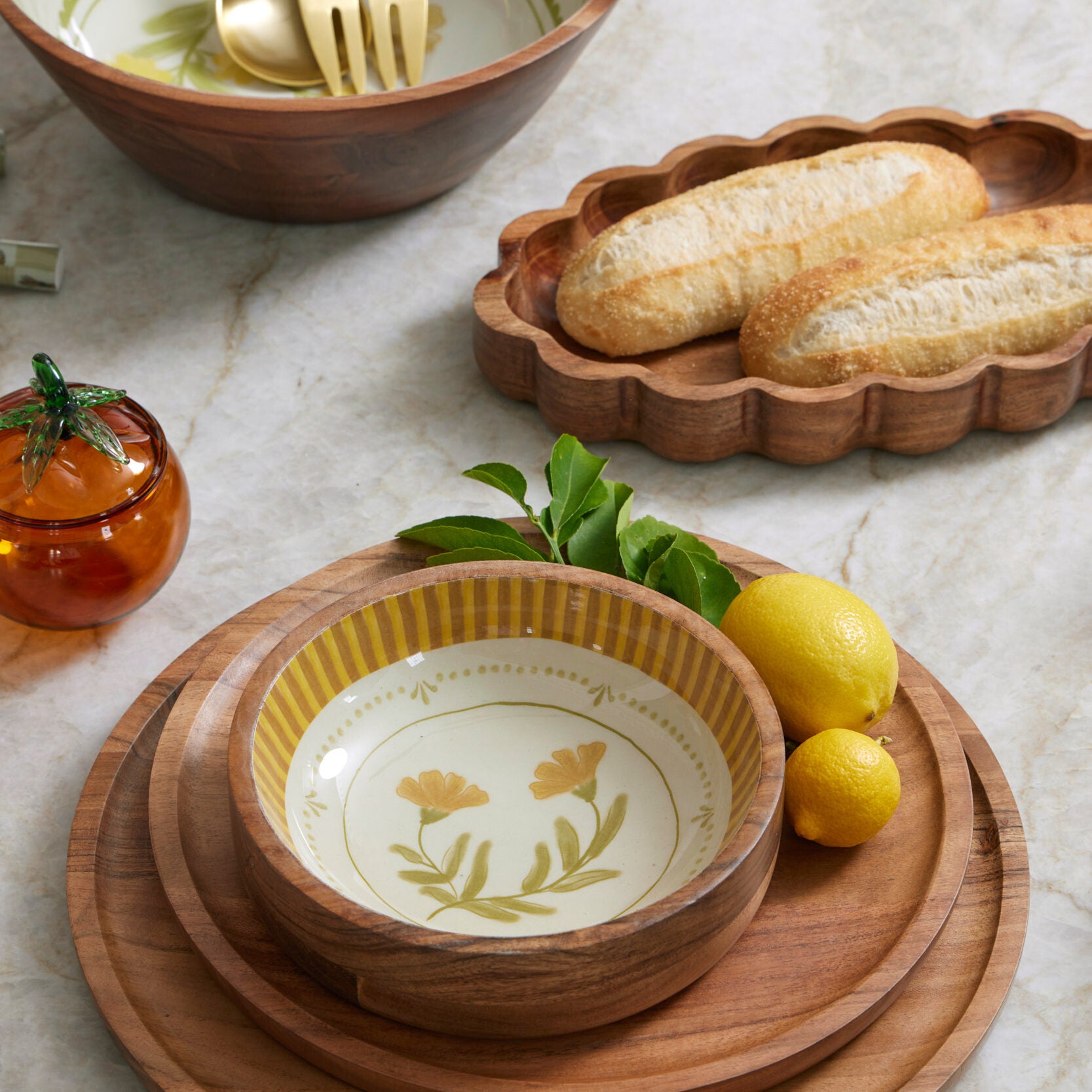 Wooden bowl with floral design on a marble surface with bread and lemons.