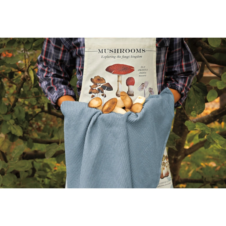 Person wearing a mushroom-themed apron with a blue apron over it, standing in a forest setting.