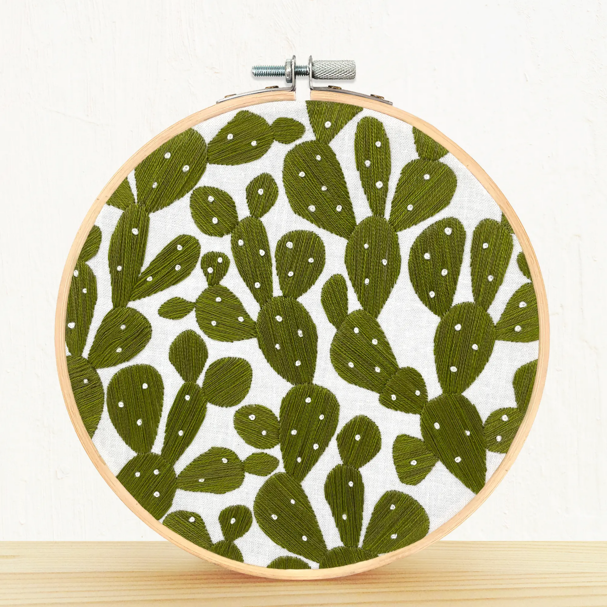 Embroidery DIY Craft kit completed loom  Prickly pears. The background is white and it is placed on a pine shelf.