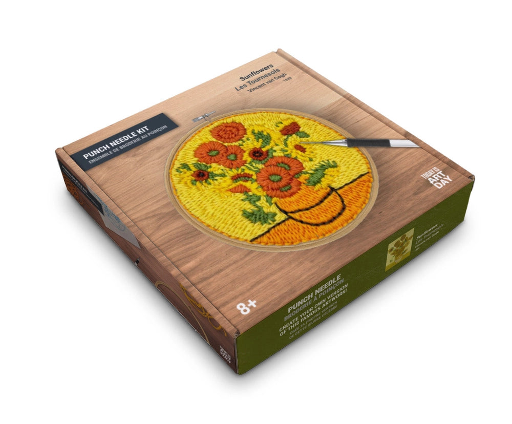 A boxed punch needle kit shown at an angle on a white background. The box features a wood-grain style design with a circular preview of a sunflowers patchwork design in yellow, orange, red, and green, plus a small embroidery tool illustration.