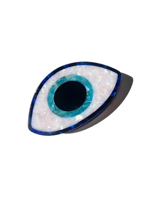 Decorative eye-shaped hair clip with blue center and white border on a white background