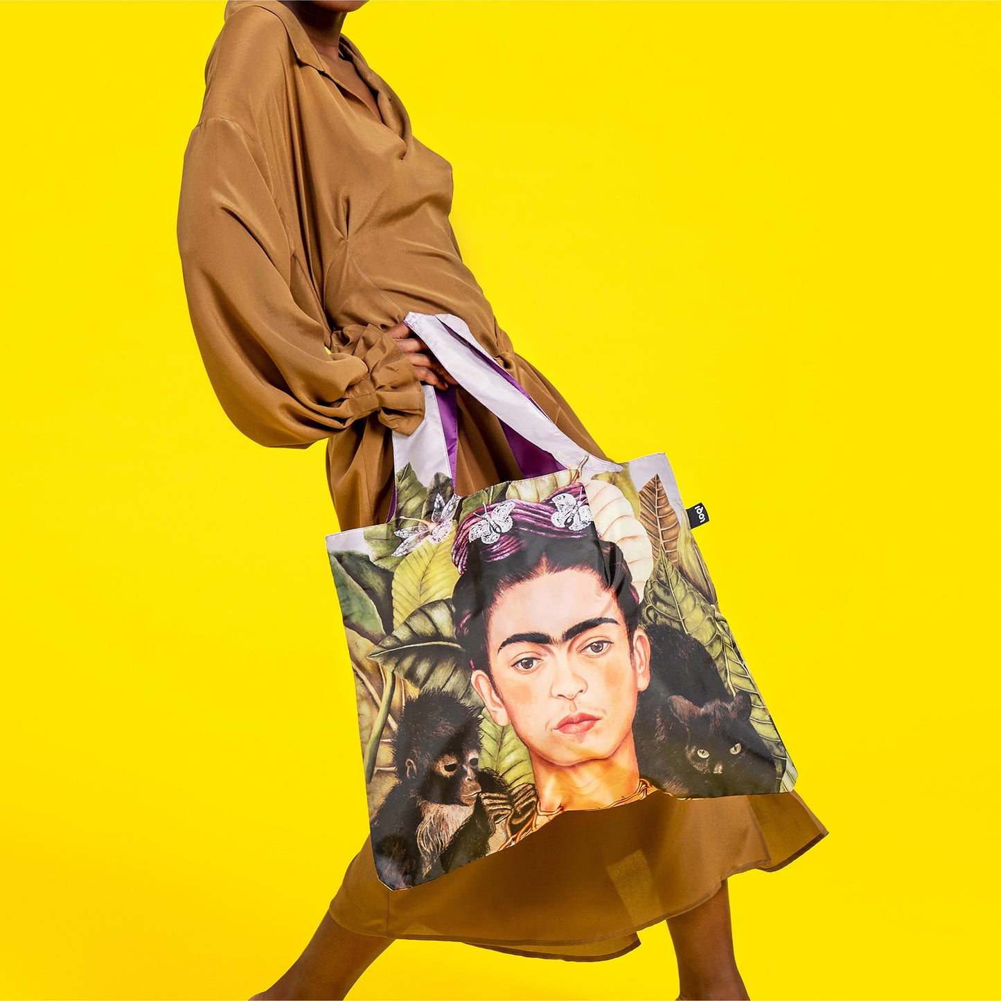Person holding a tote bag with a portrait design on a yellow background